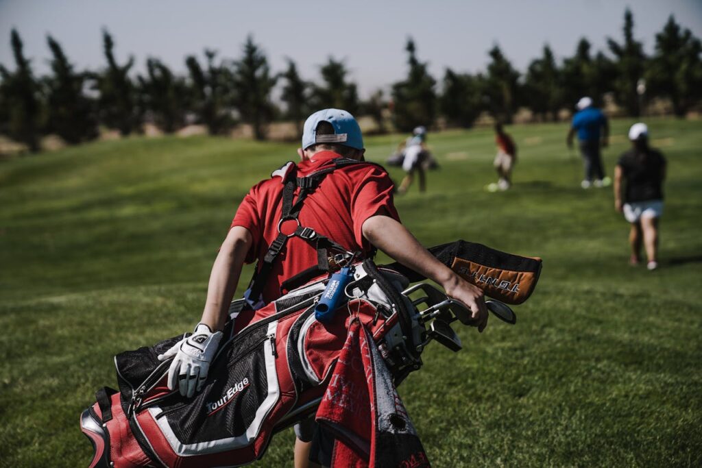 Man Walking Carrying Black and Red Golf Bag on Green Grass Field